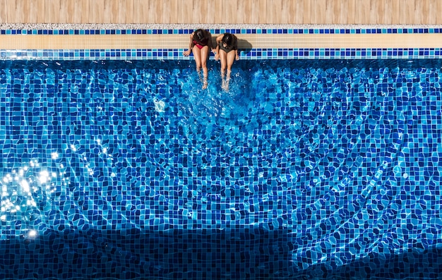 Zwei Frauen, die am Swimmingpool sich entspannen und sitzen.