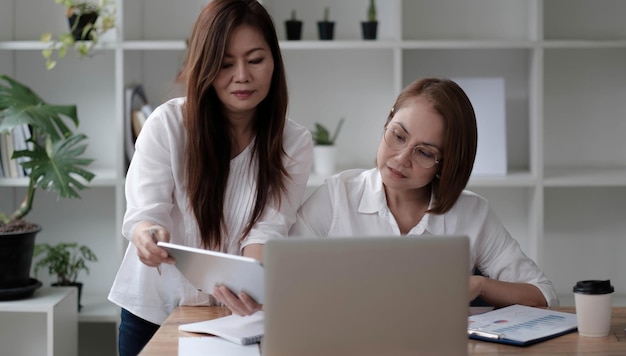 Zwei Frauen, die Dokumente analysieren, während sie auf einem Tisch im Büro sitzen Frauenführungskräfte bei der Arbeit im Büro, die etwas Papierkram besprechen