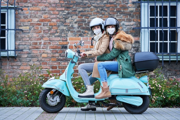 zwei Frauen, die Masken tragen und auf dem Roller pendeln