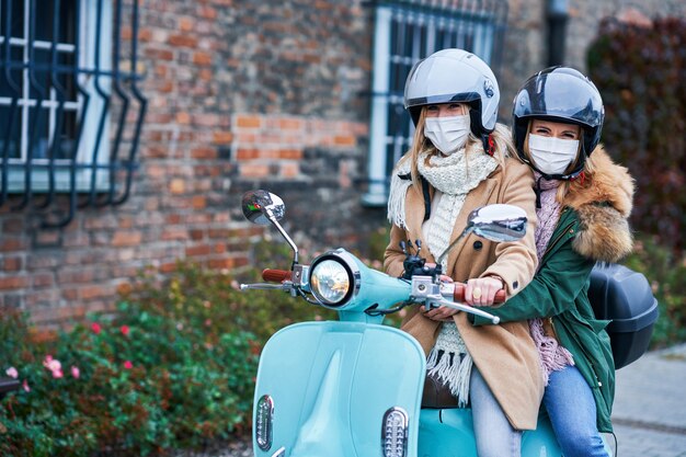 zwei Frauen, die Masken tragen und auf dem Roller pendeln