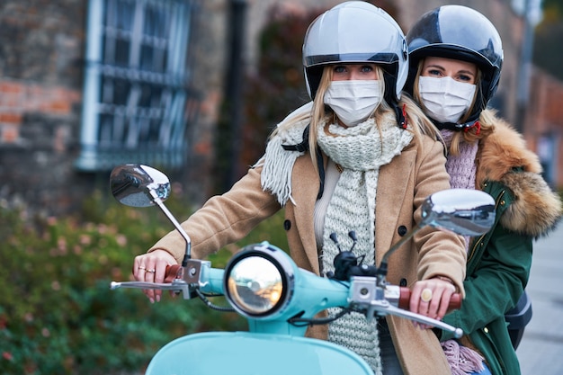 zwei Frauen, die Masken tragen und auf dem Roller pendeln