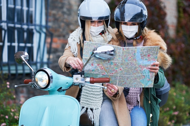 zwei Frauen, die Masken tragen und eine Karte halten, während sie mit dem Roller pendeln