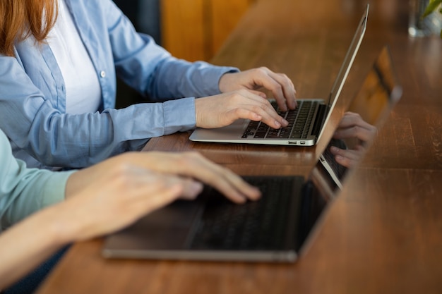 Zwei Frauen, die Text auf einem Laptop eingeben Europäische Geschäftsfrauen, die E-Mails von einem Computer senden
