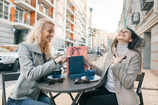 Zwei Frauen im Straßencafé mit Einkaufstüten und Tasse Kaffee