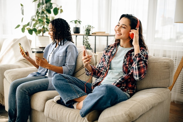 Foto zwei frauen in kopfhörern entspannen sich auf dem sofa