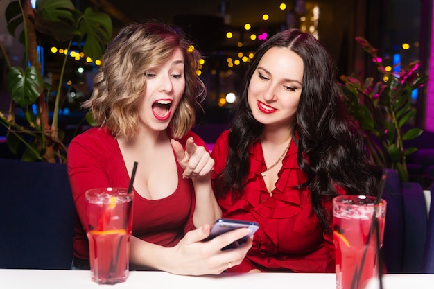 Zwei Frauen in roten Kleidern trinken Cocktails und feiern in einem Nachtclub oder einer Bar