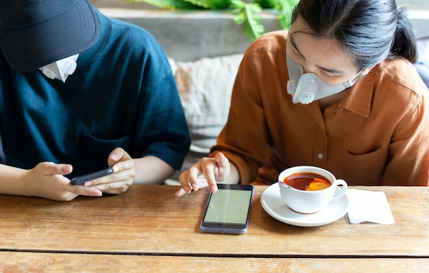 Zwei Frauen in Schutzmaske verhindern, dass Covid-19 im Café ein Handy benutzt und Zitronentee trinkt.