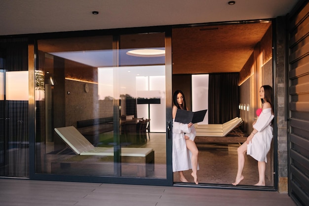 Zwei Frauen in weißen Kleidern stehen vor einer Glastür mit einem großen Fenster, auf dem „Spa“ steht.