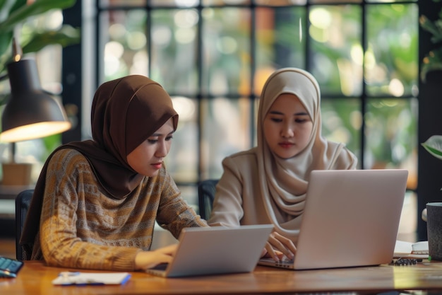 Zwei Frauen mit Hijab arbeiten im Büro an einem Laptop