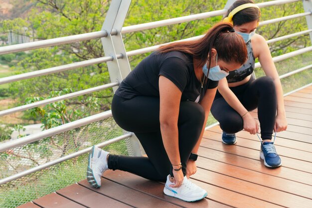 Zwei Frauen mit Schutzmasken binden ihre Schnürsenkel, um sich auf einen Lauf vorzubereiten.