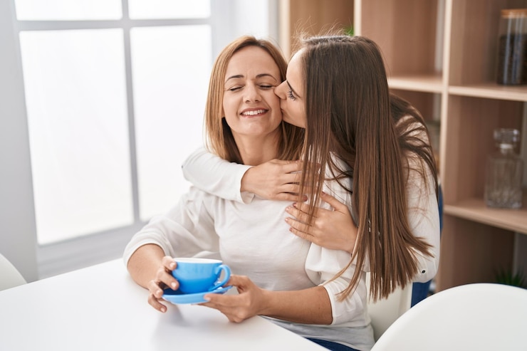 Foto zwei frauen, mutter und tochter, umarmen sich zu hause beim kaffeetrinken