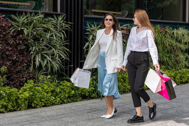 Zwei Frauen plaudern auf der Straße mit Taschen nach dem Einkaufen in einem Gewerbegebiet