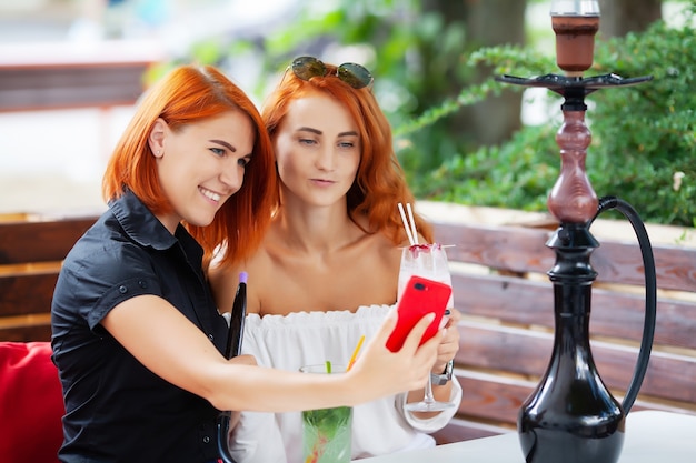 Zwei Frauen rauchen eine Wasserpfeife und genießen Cocktails in einem Café auf der Straße.