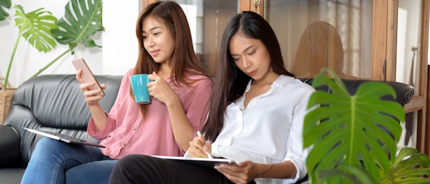 Zwei Frauen sitzen auf Sofa, mit Smartphone und Tablet