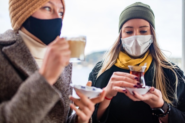 Zwei frauen trinken türkischen tee und salep, während sie eine medizinische maske tragen