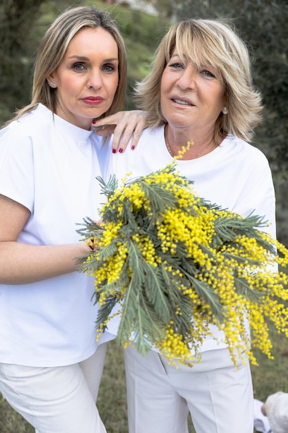 Zwei Frauen umarmen sich mit einem Bouquet gelber Mimosas