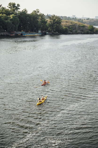 Zwei Frauen und ein Mann, die am Sommermorgen im Fluss Kajak fahren. Rückansicht