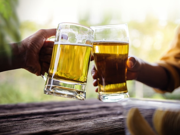 Zwei Freunde, die Beifall mit Gläsern machen und Bier am Balkon im Sommer trinken