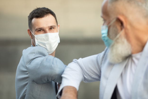 Zwei freunde mit gesichtsmaske begrüßen sich mit dem ellbogen auf der straße