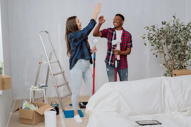 Zwei Freunde renovieren die Wände eines Schlafsaals und streichen Wände mit Farbrollern in den Händen