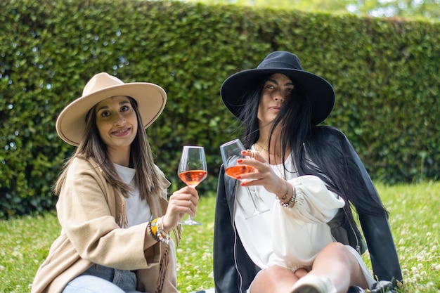 Zwei Freunde sitzen auf dem Rasen ihres Gartens, halten zwei Gläser Champagner und schauen in die Kamera