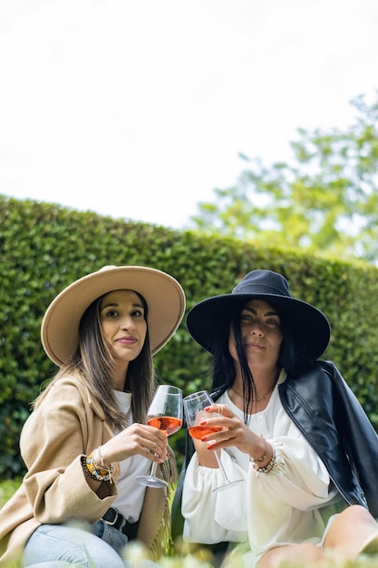 Zwei Freunde sitzen auf dem Rasen ihres Gartens, halten zwei Gläser Champagner und schauen in die Kamera