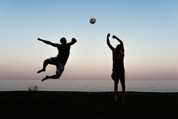 Zwei Freunde spielen Fußball am Strand.