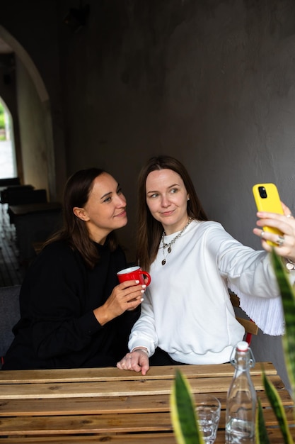 Zwei Freundinnen amüsieren sich draußen im Café und machen ein Selfie auf einem Smartphone