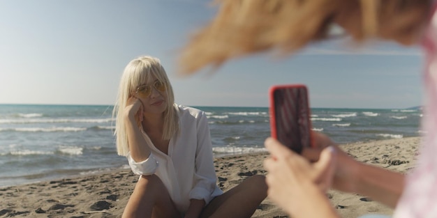 Zwei Freundinnen fotografieren mit Smartphone am leeren Strand während des Herbsttages