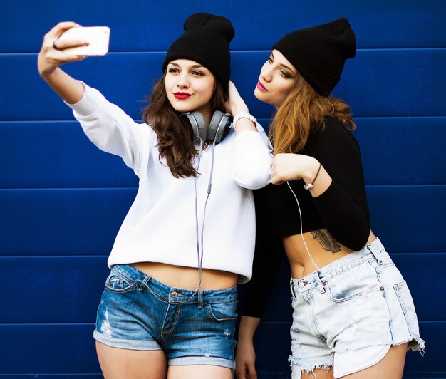 Zwei Freundinnen im Teenageralter in Hipster-Outfit im Freien machen Selfie auf einem Telefon.