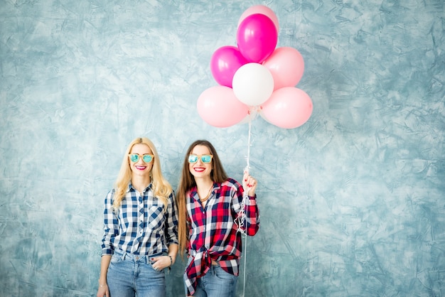 Zwei Freundinnen in karierten Hemden, die sich mit Luftballons auf dem blauen Wandhintergrund amüsieren