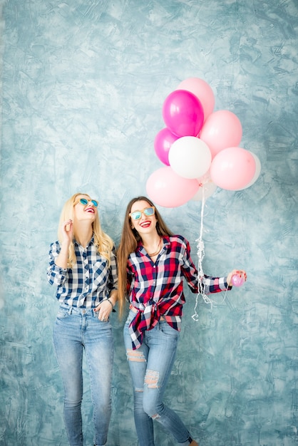 Zwei Freundinnen in karierten Hemden, die sich mit Luftballons auf dem blauen Wandhintergrund amüsieren