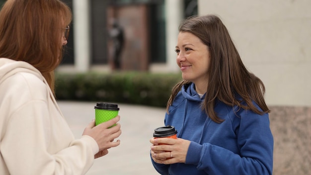 Zwei Freundinnen, junge Studenten, unterhalten sich und trinken Kaffee im Freien auf dem Campus.
