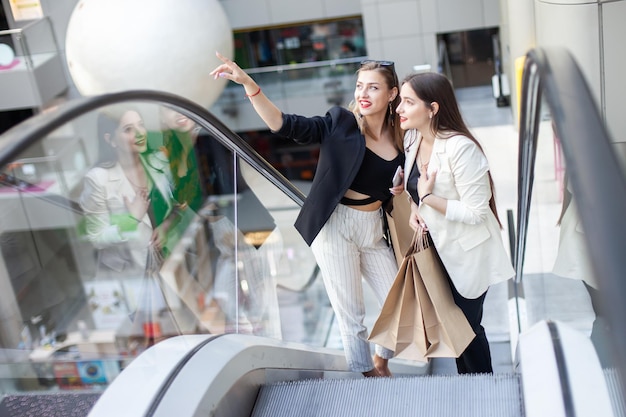 Zwei Freundinnen mit Einkaufstüten klettern die Rolltreppe im Einkaufszentrum hinauf