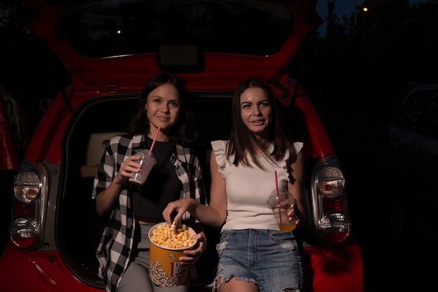 Zwei Freundinnen mit Popcorn sitzen im Auto, während sie sich einen Film im Kino ansehen Selektiver Fokus Unterhaltung Freizeitaktivitäten Hobby-Konzept