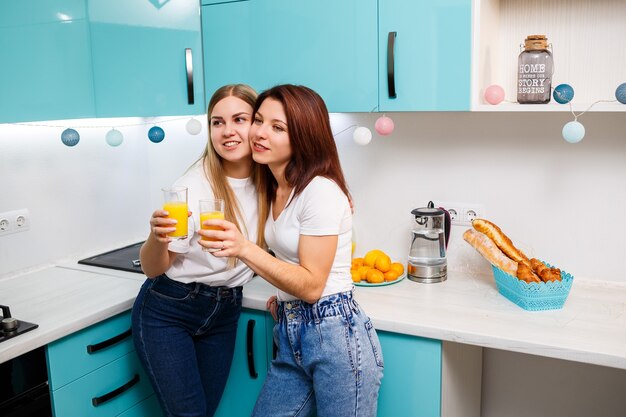 Zwei Freundinnen stehen in der Küche und trinken Orangensaft. Freundinnen plaudern und teilen Geheimnisse in der Küche, beim Frühstück