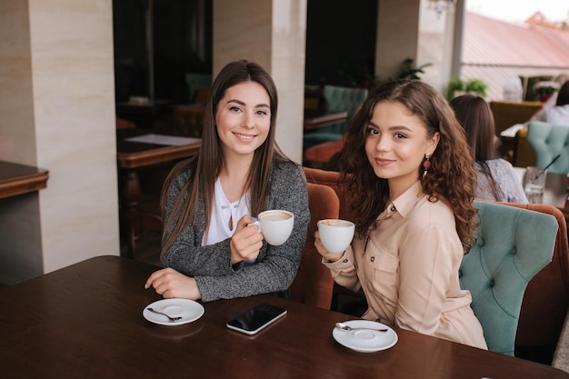 Zwei Freundinnen trinken Kaffee im Restaurant und sprechen Schöne Frauen treffen sich im Café Ende der Quarantäne Attraktive Mädchen auf der Terrasse