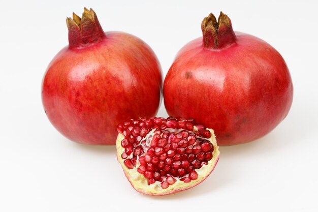 Zwei frische rote Granatapfelfrüchte mit einem geschälten Stück auf weißem Hintergrund