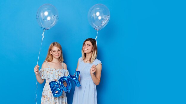 Zwei fröhliche Frauen mit blauen Luftballons und Ballon mit der Aufschrift Junge blauer Hintergrund Platz für Text