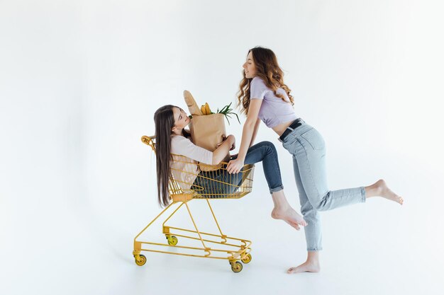 Zwei fröhliche junge Frauen in farbenfrohen trendigen Outfits lächeln und haben Spaß mit Trolley