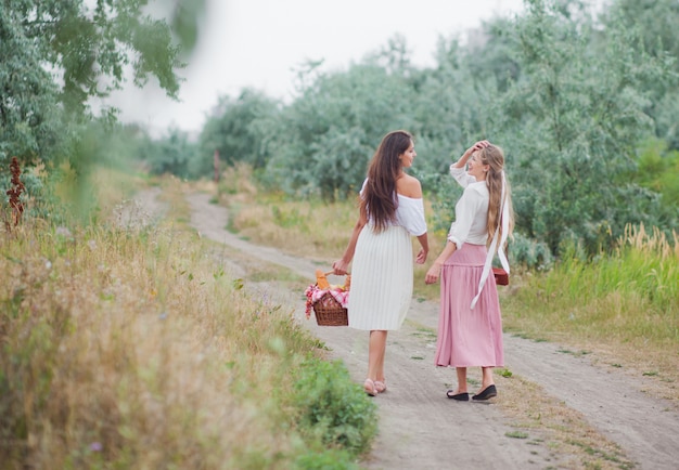 Zwei fröhliche junge Frauen in Retro-Kleidung gehen mit einem Picknickkorb den Treppenabsatz entlang und unterhalten sich.