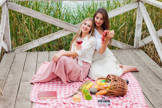 Zwei fröhliche junge Frauen machen an einem Sommertag ein Picknick im Freien.