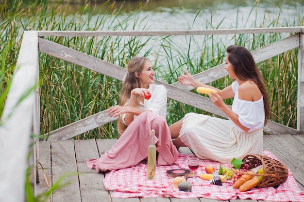 Zwei fröhliche junge Frauen machen an einem Sommertag ein Picknick im Freien.