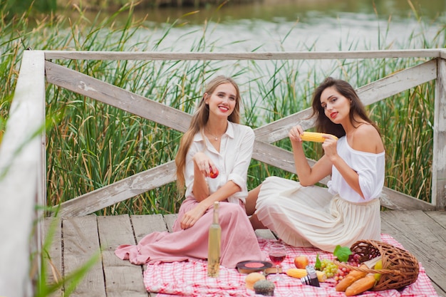 Zwei fröhliche junge Frauen machen an einem Sommertag ein Picknick im Freien.