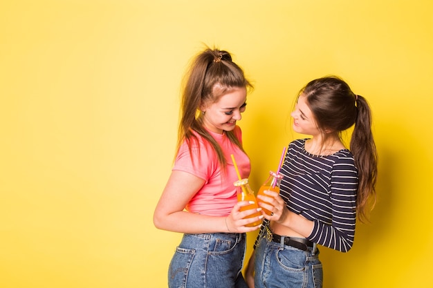 Zwei fröhliche junge Schönheitsmädchen des jungen Hipsters, die zusammen auf gelbem Hintergrund aufwerfen