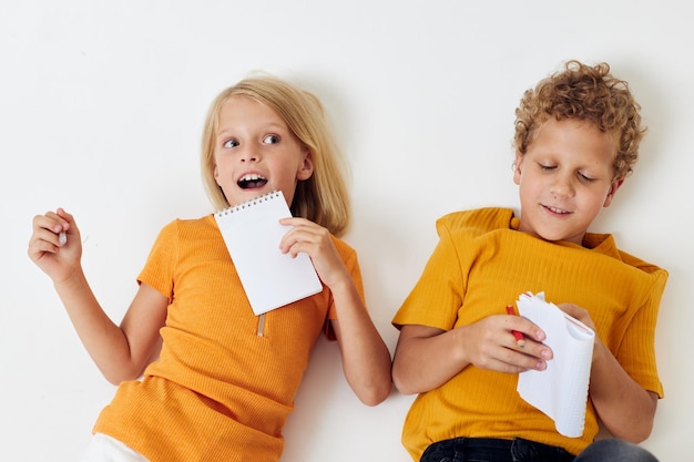 Zwei fröhliche Kinder zeichnen in Notizbüchern, die unverändert auf dem hellen Hintergrund des Bodens liegen