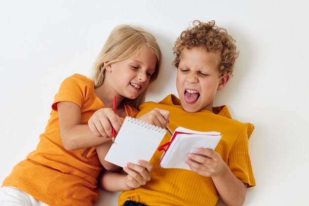 Zwei fröhliche Kindergefühle, die zusammen Notizblock und Bleistifte Kindheitslebensstil unverändert zeichnen