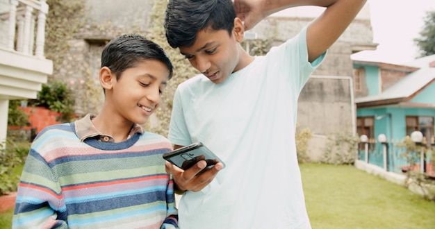 Zwei fröhliche kleine Jungs aus Indien surfen im Smartphone im Freien