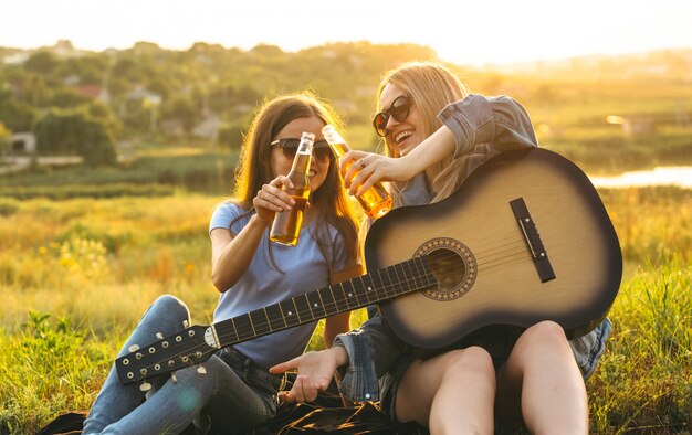 Zwei fröhliche Mädchen und junge Freunde mit Sonnenbrille, Bier trinken und gemeinsam die Zeit bei Sonnenuntergang genießen.