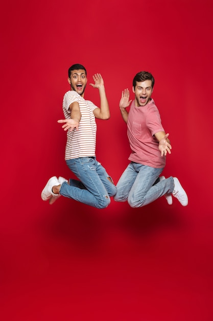Zwei fröhliche Männerfreunde, die isoliert über rote Wand springen